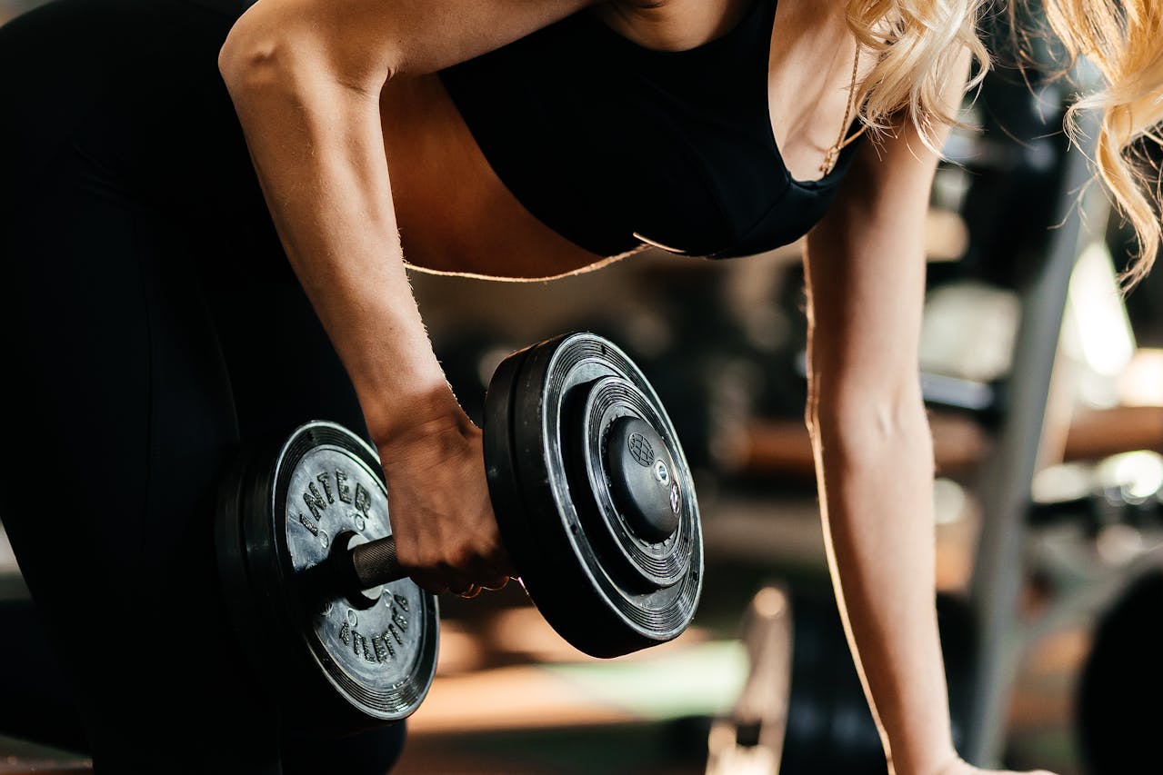 Middle aged woman wearing black top and tights lifting a heavy dumbbell
