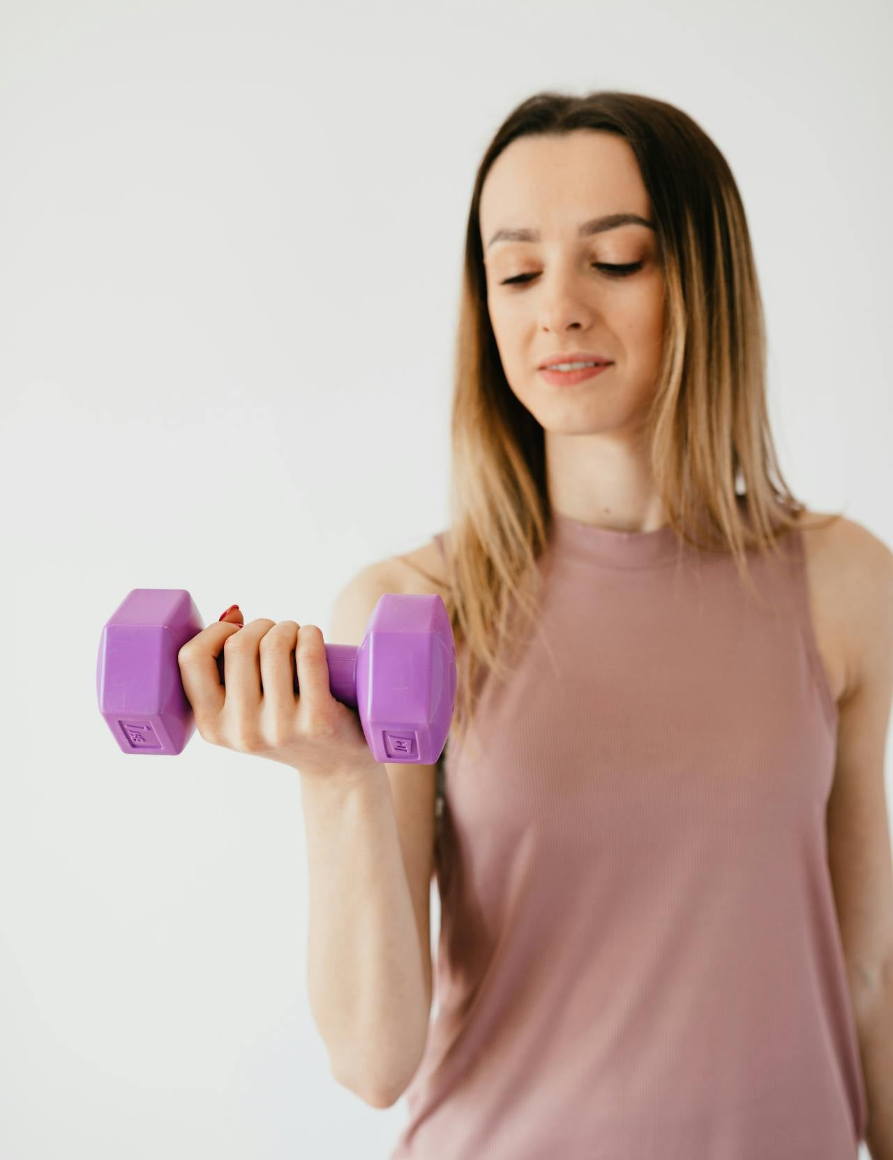 Woman in activewear lifting a purple dumbbell during a strength training workout against a neutral background.