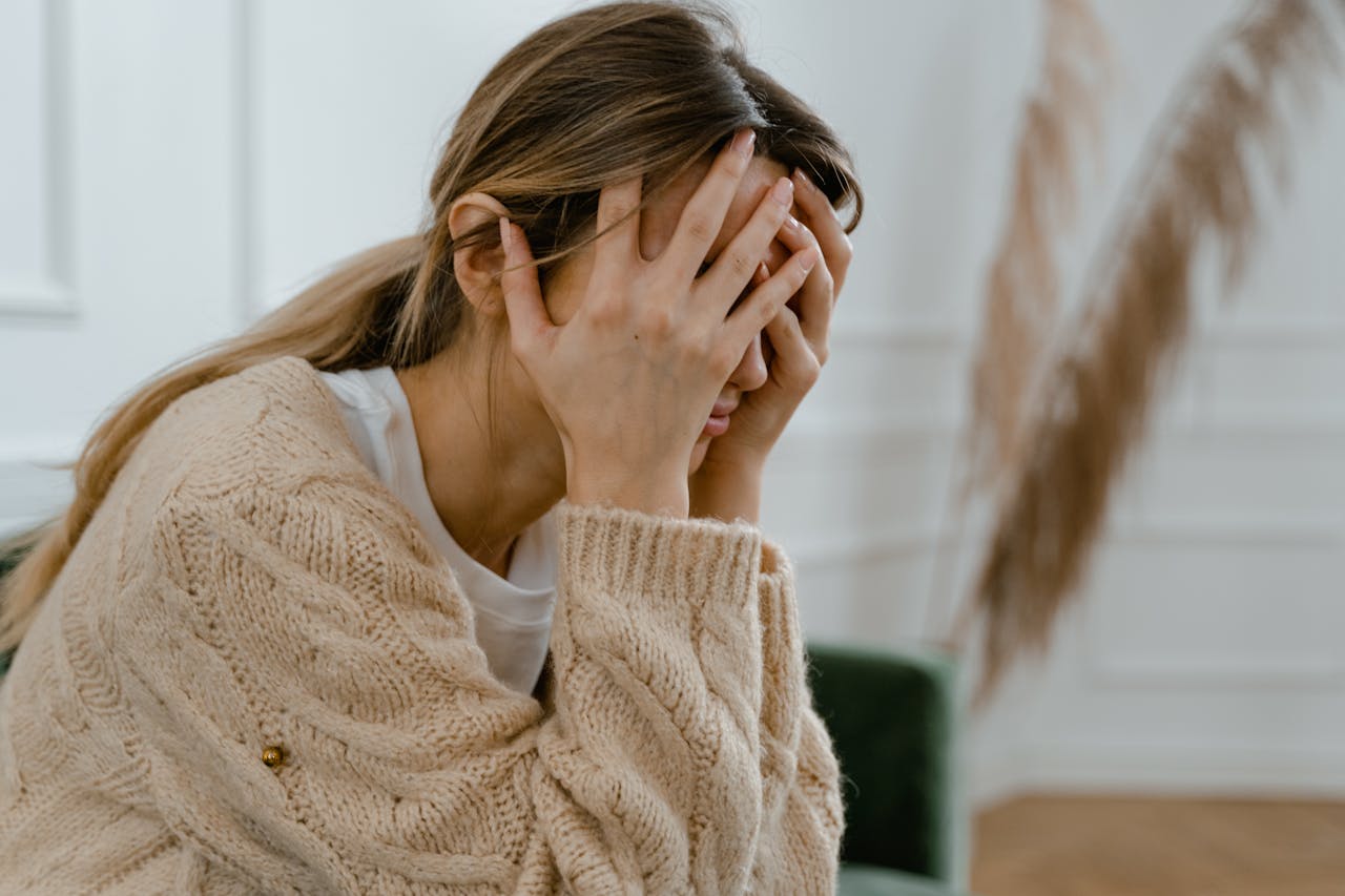 Woman sitting indoors holding her head in her hands, appearing overwhelmed or stressed