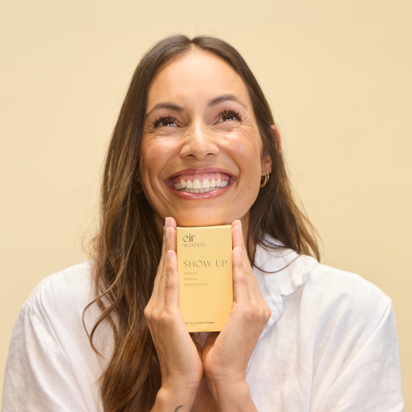 Woman holding a gold box with 'Show Up' branding against a beige background