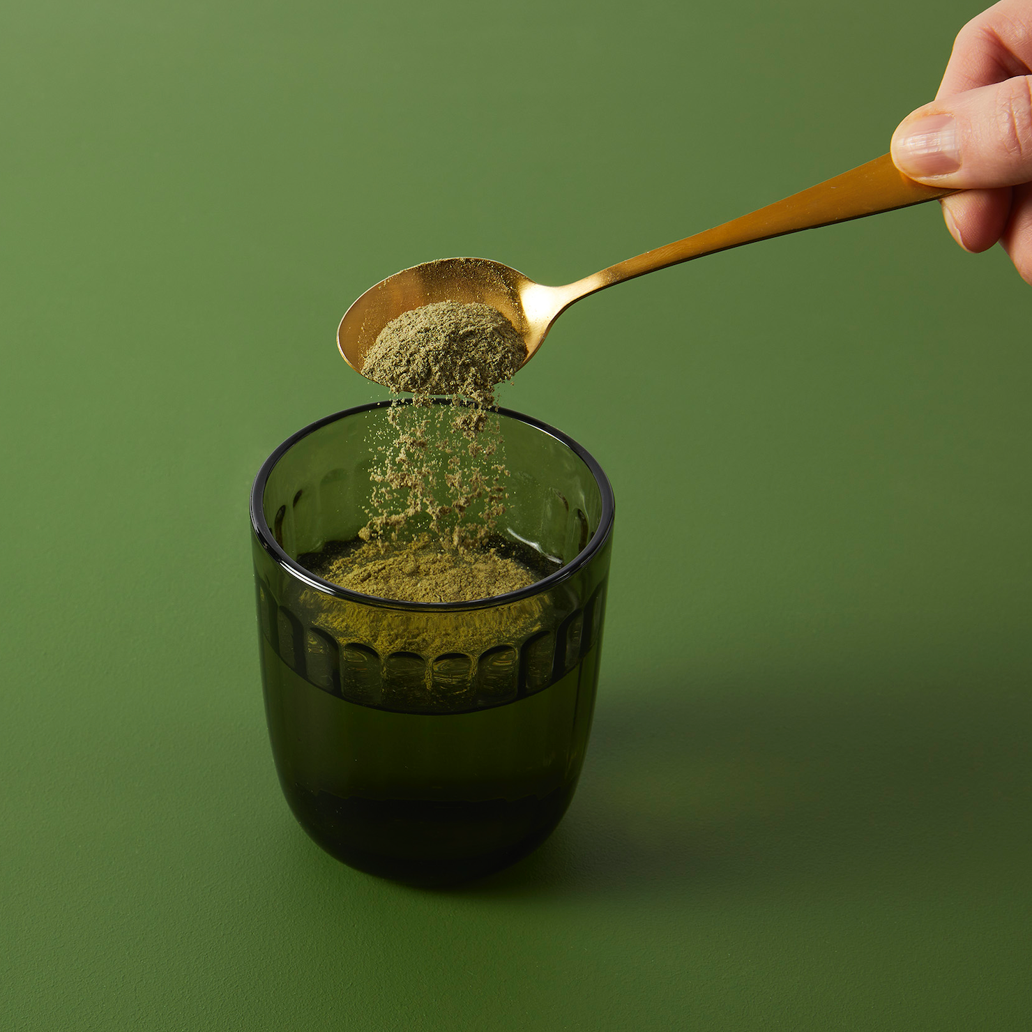 Green powder on spoon being tipped into green glass